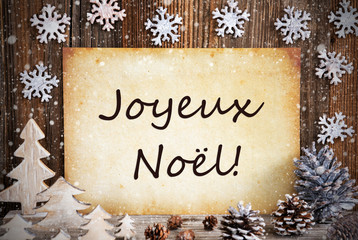 Fototapeta na wymiar Old Paper With French Text Joyeux Noel Means Merry Christmas. Christmas Decoration Like Tree, Fir Cone And Snow. Brown Wooden Background