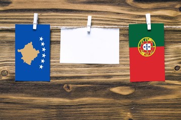 Hanging flags of Kosovo and Portugal attached to rope with clothes pins with copy space on white note paper on wooden background.Diplomatic relations between countries.