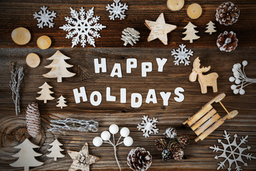 White Letters Building The Word Happy Holidays. Wooden Christmas Decoration Like Tree, Sled, Star And Fir Cone. Brown Wooden Background