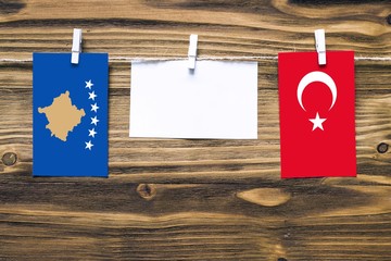Hanging flags of Kosovo and Turkey attached to rope with clothes pins with copy space on white note paper on wooden background.Diplomatic relations between countries.