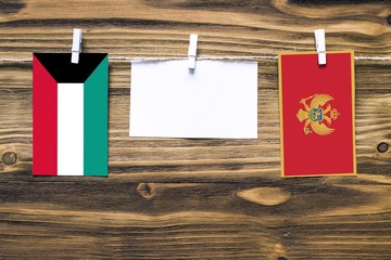 Hanging flags of Kuwait and Montenegro attached to rope with clothes pins with copy space on white note paper on wooden background.Diplomatic relations between countries.