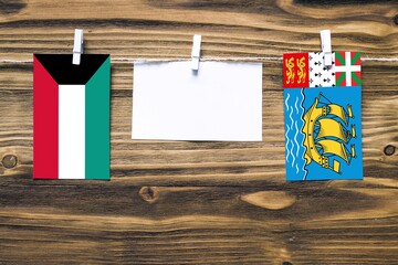 Hanging flags of Kuwait and Saint Pierre And Miquelon attached to rope with clothes pins with copy...