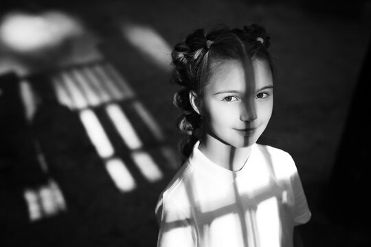 cute little thoughtful girl standing at the night playground. shadows from gungle gym falling on her face and body. black and white photo