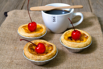 egg tart in aluminum foil cup with red cherry and coffee on wood table
