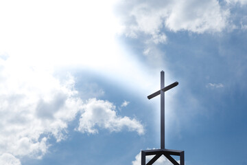 A Christian crucifix atop a church silhouetted by rays of light from above.