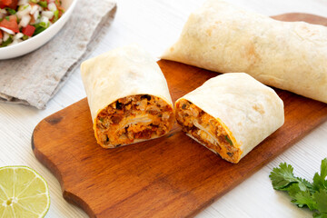 Homemade chorizo breakfast burritos on a rustic wooden board on a white wooden table, side view....