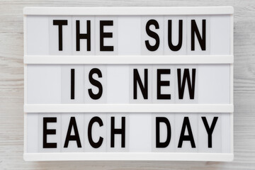 Obraz premium 'The sun is new each day' words on a lightbox on a white wooden surface, top view. Overhead, from above, flat lay. Close-up.