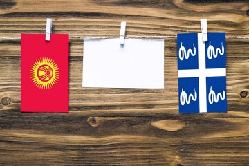 Hanging flags of Kyrgyzstan and Martinique attached to rope with clothes pins with copy space on white note paper on wooden background.Diplomatic relations between countries.