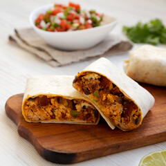 Homemade chorizo breakfast burritos on a rustic wooden board on a white wooden background, low...
