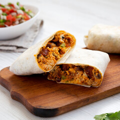 Homemade chorizo breakfast burritos on a rustic wooden board on a white wooden table, side view. Close-up. - obrazy, fototapety, plakaty