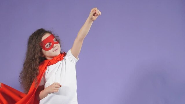 Superhero concept. Little girl in red mask and cloak raised arms up, imagines herself as hero