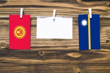 Hanging flags of Kyrgyzstan and Nauru attached to rope with clothes pins with copy space on white note paper on wooden background.Diplomatic relations between countries.