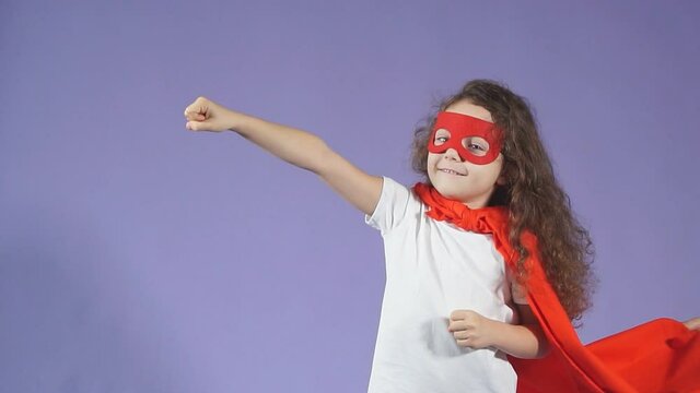 Positive little girl enthusiastically raised arms up, dressed in red mask and red cloak. Spaceman concept
