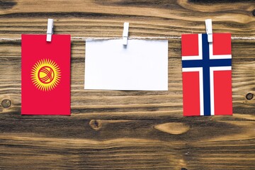 Hanging flags of Kyrgyzstan and Norway attached to rope with clothes pins with copy space on white...