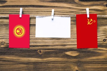 Hanging flags of Kyrgyzstan and Soviet Union attached to rope with clothes pins with copy space on white note paper on wooden background.Diplomatic relations between countries.