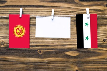 Hanging flags of Kyrgyzstan and Syria attached to rope with clothes pins with copy space on white...