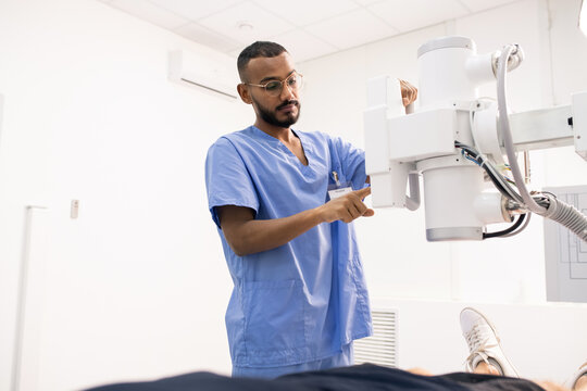 Bearded young mixed-race man in blue uniform using new medical equipment
