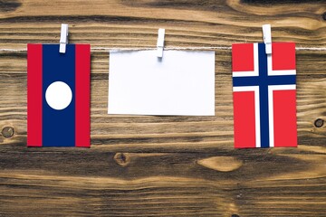 Hanging flags of Laos and Norway attached to rope with clothes pins with copy space on white note...
