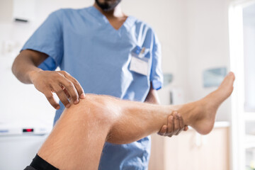 Contemporary mixed-race professional touching sick knee of his patient