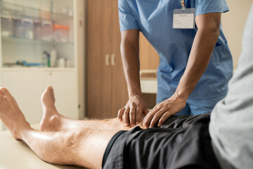 Obraz na płótnie Canvas Hands of mixed-race clinician in blue uniform massaging one of legs of patient