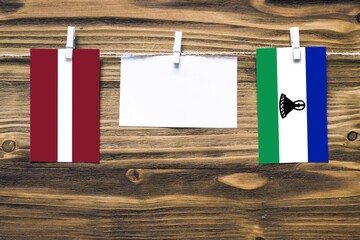 Hanging flags of Latvia and Lesotho attached to rope with clothes pins with copy space on white...