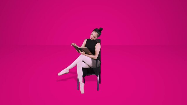 Ballet dancer sitting on the chair while reading a references book in the studio. Shot in 4k resolution with pink background