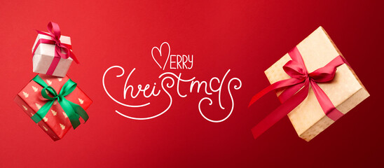 Christmas shopping concept. Gift boxes are flying in the air and hand-lettering Merry Christmas on a red background.
