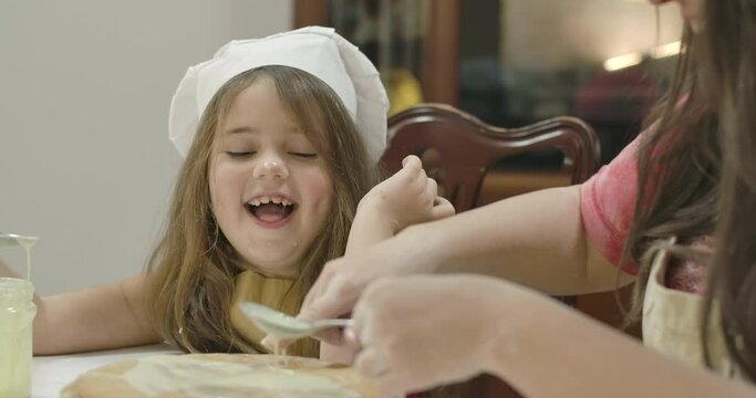 Adult Caucasian woman touching daughter's nose with a finger in sweetened condensed milk. Little pretty girl cooking with mother at home. Happy family baking cakes. Cinema 4k footage ProRes HQ.