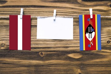 Hanging flags of Latvia and Swaziland attached to rope with clothes pins with copy space on white...