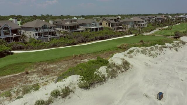 Aerial: Drone panning over people at beach by houses and ponds against sky during sunny summer weekend - Kiawah Island, SC
