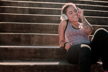 Cheerful young woman listening to music on stairs outdoors
