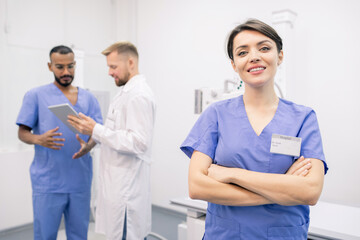 Happy young cross-armed clinician in uniform standing in front of camera