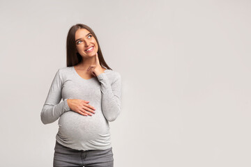 Happy Pregnant Woman Thinking Standing Over Gray Studio Background