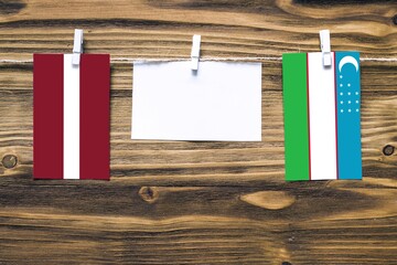 Hanging flags of Latvia and Uzbekistan attached to rope with clothes pins with copy space on white note paper on wooden background.Diplomatic relations between countries.