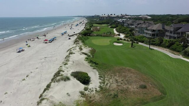 Aerial: Drone moving over green golf course amidst houses and beach against sky on sunny day - Kiawah Island, SC