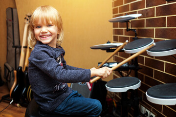 Little caucasian girl drummer playing the electronic drum kit. Girl learns to play drums in music...