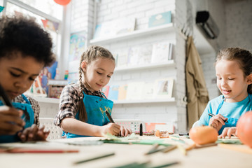 Two cute diligent girls and African boy drawing with highlighters by desk