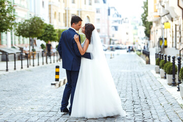 Fototapeta premium Gorgeous wedding couple walking in the city. Groom in a stylish suit and bride in a beautiful white dress, the couple is walking the streets of the city on their wedding day. Together. Wedding concept
