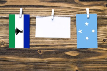 Hanging flags of Lesotho and Micronesia attached to rope with clothes pins with copy space on white...