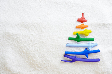 Flat lay stylized Christmas tree made of small twigs painted in rainbow colors on snow background. Space for text