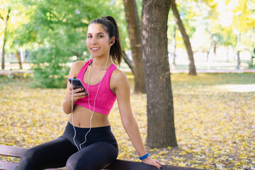 Physically fit woman sitting in the park, holding her phone