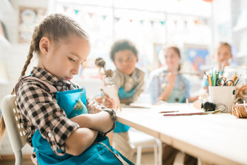 Offended girl crossing arms while sitting by desk on background of classmates