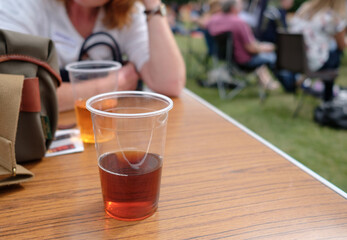 Part drunken pint of beer seen on a festival outdoor table, with members of the public seen listening to a live music event in summer.
