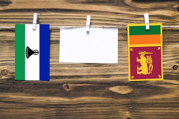 Hanging flags of Lesotho and Sri Lanka attached to rope with clothes pins with copy space on white...