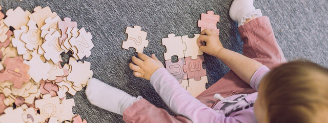 Child make puzzle joining pieces at floor search right letters. Question for right solution,...