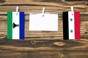 Hanging flags of Lesotho and Syria attached to rope with clothes pins with copy space on white note...