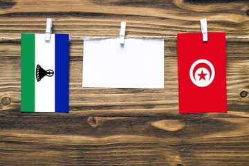 Hanging flags of Lesotho and Tunisia attached to rope with clothes pins with copy space on white...
