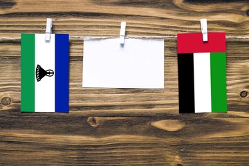 Hanging flags of Lesotho and United Arab Emirates attached to rope with clothes pins with copy...