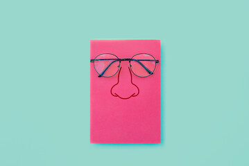 Glasses placed on pink book, Nose icon on book cover, On blue background