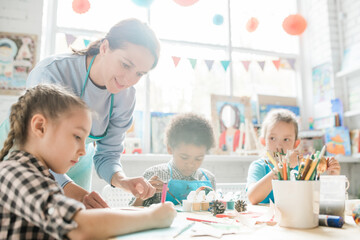 Happy young teacher looking at Christmas drawing of little schoolgirl